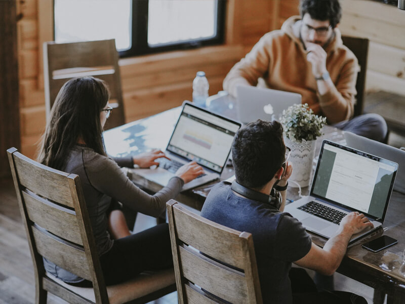 Equipe trabalhando em conjunto com seus laptops em uma mesa.